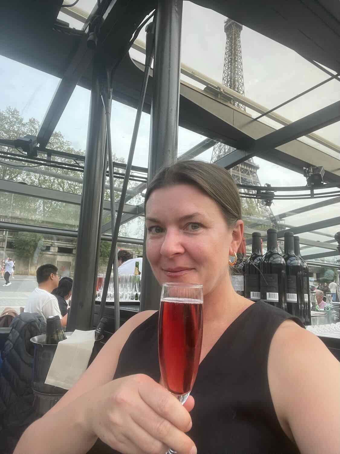 A woman enjoying a glass of rosé wine at a restaurant in Paris, with the Eiffel Tower visible in the background.