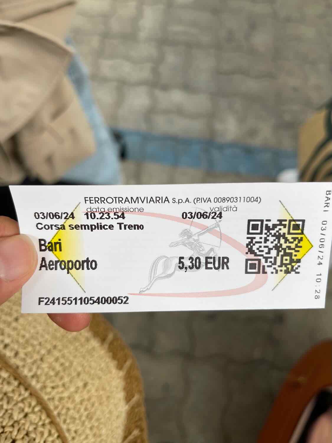 A train ticket from Bari to Aeroporto costing 5.30 EUR, issued by Ferrovie del Nord Barese. The ticket is held by someone with a woven bag visible in the background.