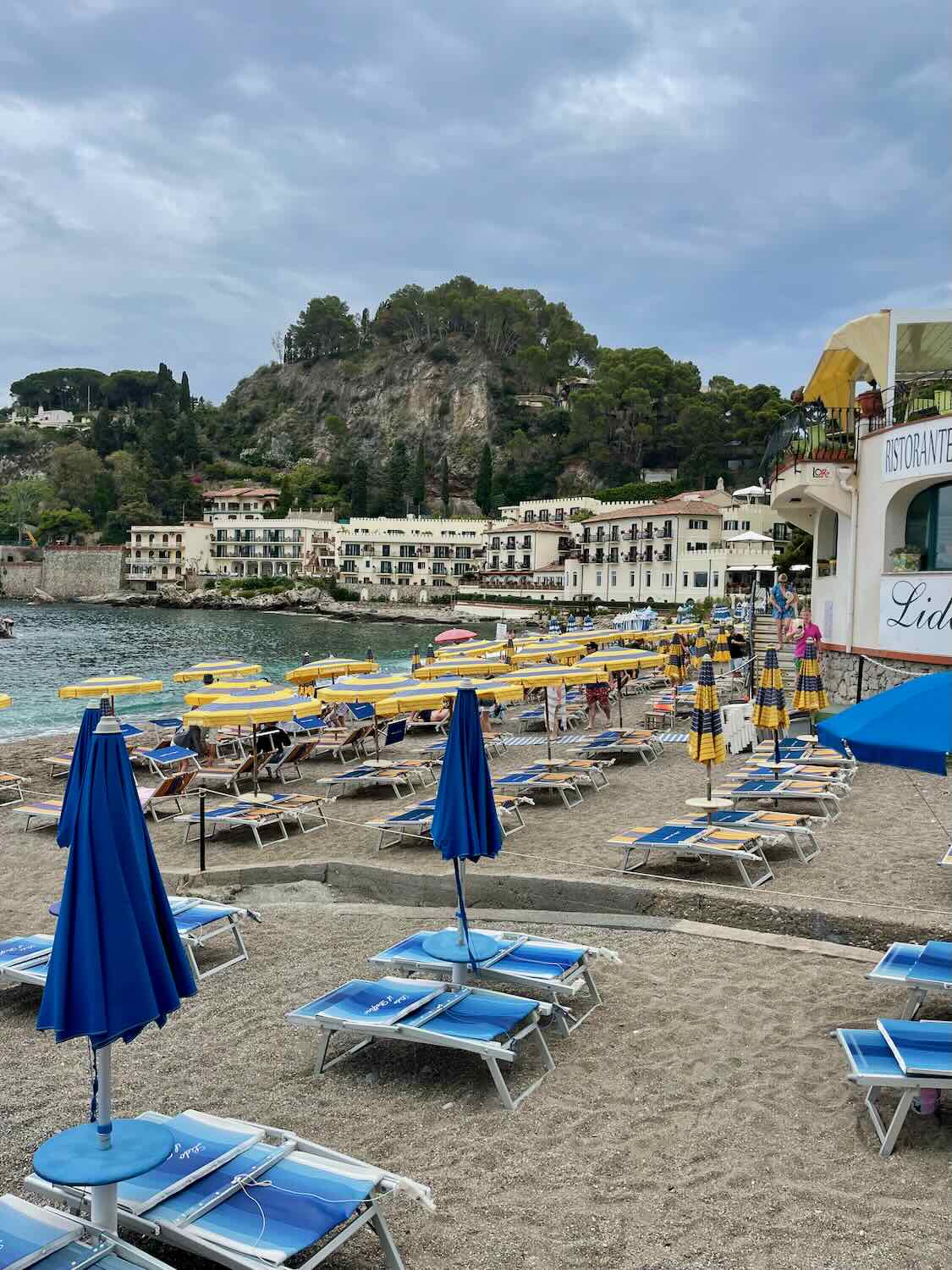 The beach in Taormina that has yellow umbrellas and blue chairs. 