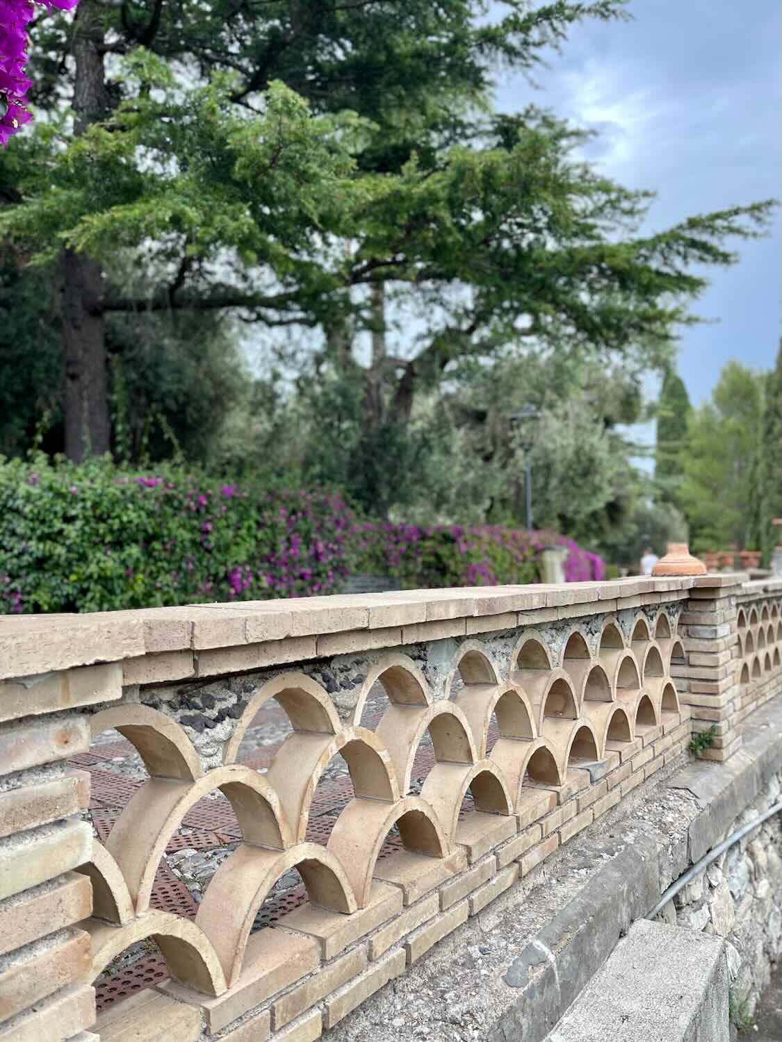 A picture of a cement fence with the Gardens in the background. 