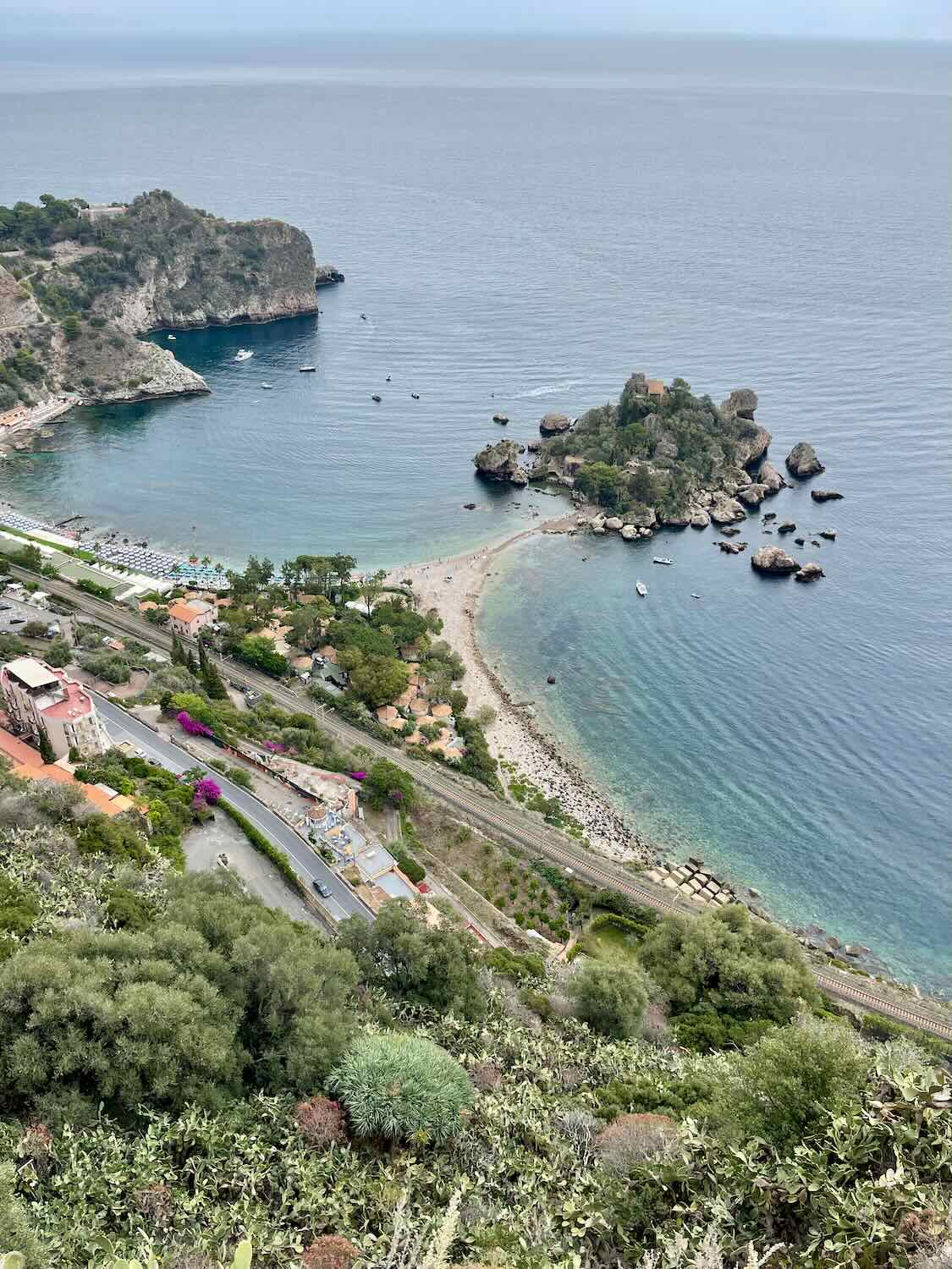 A shot of Isola Bella from above. Clear blue water and the sandy path towards the island all visible. 