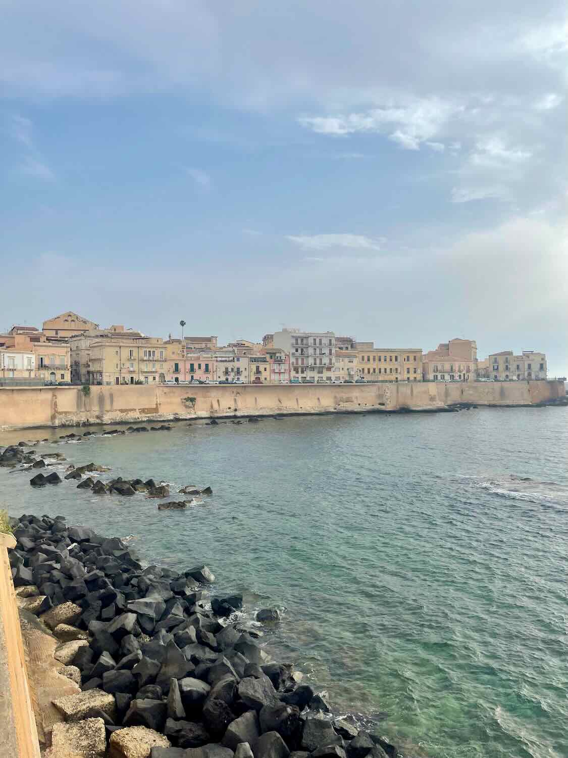 The rocky coast and beautiful colorful buildings by the sea in Siracusa