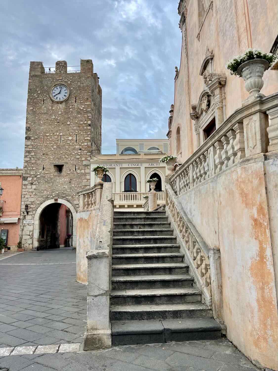 A staircase and the clock tower of Porta di Mezzo in the background. 