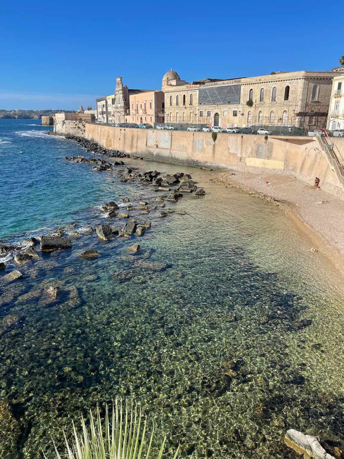 A view of crystal blue water and historic buildings in Siracusa