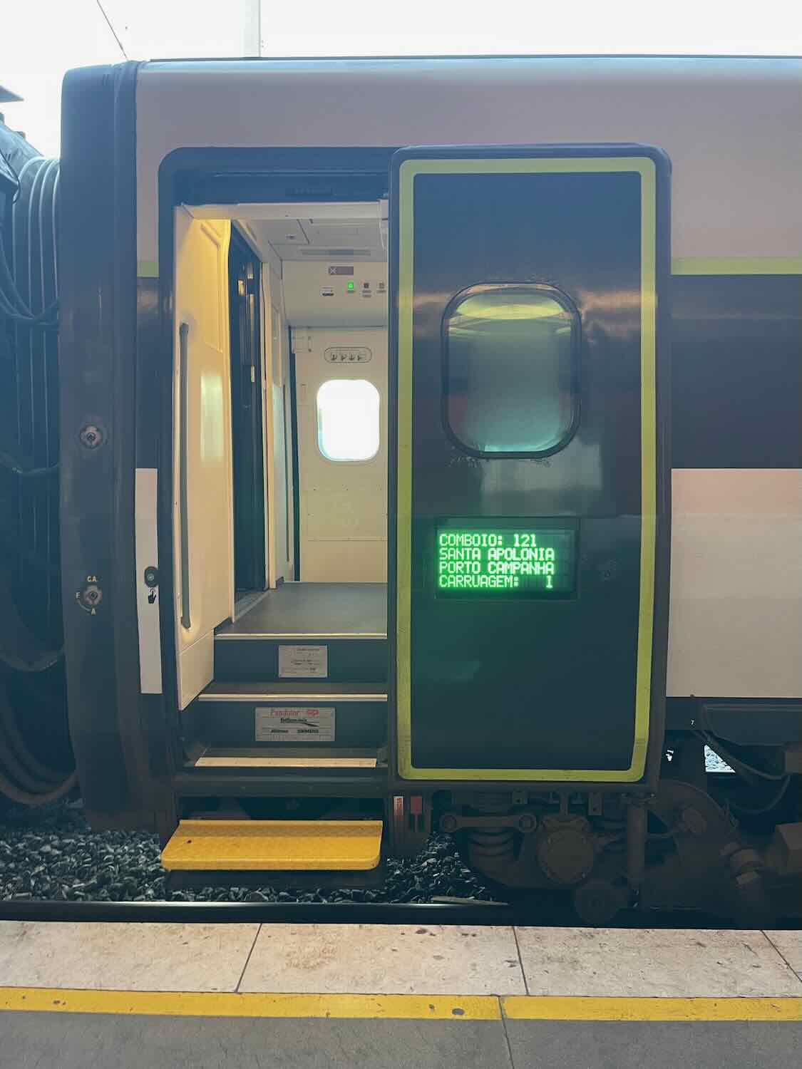 An open train door showing the interior steps with a digital sign displaying the destination as Santa Apolónia, Porto Campanha.