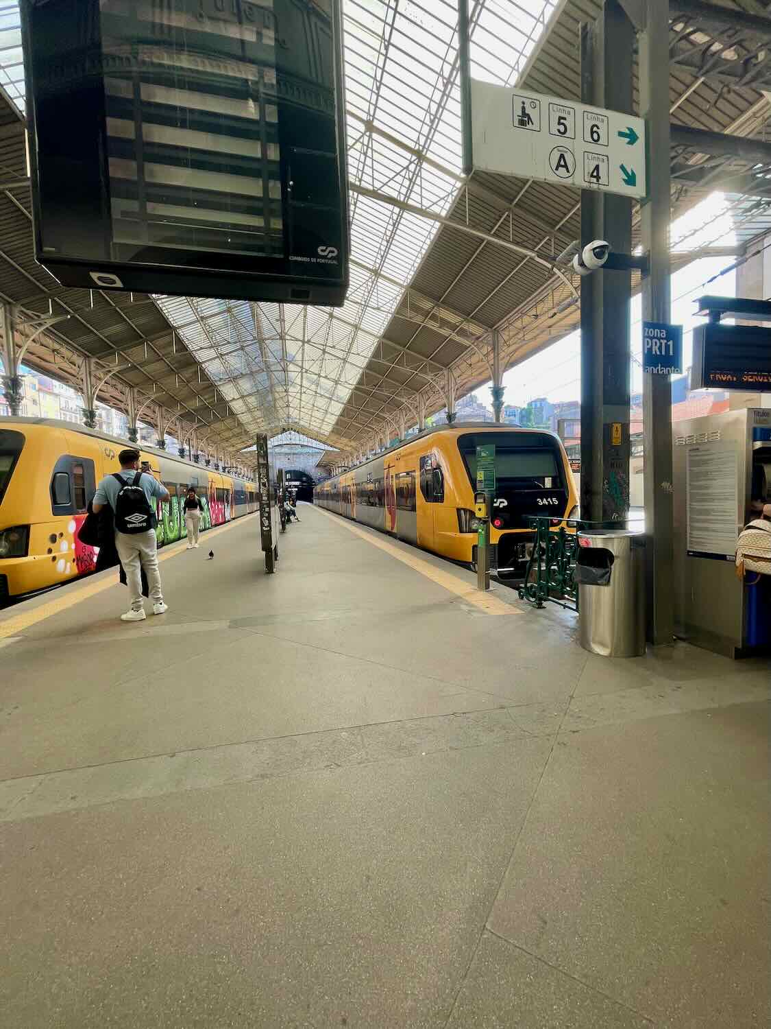  Inside a train station in Porto, with yellow trains on both sides and a high arched glass roof overhead.