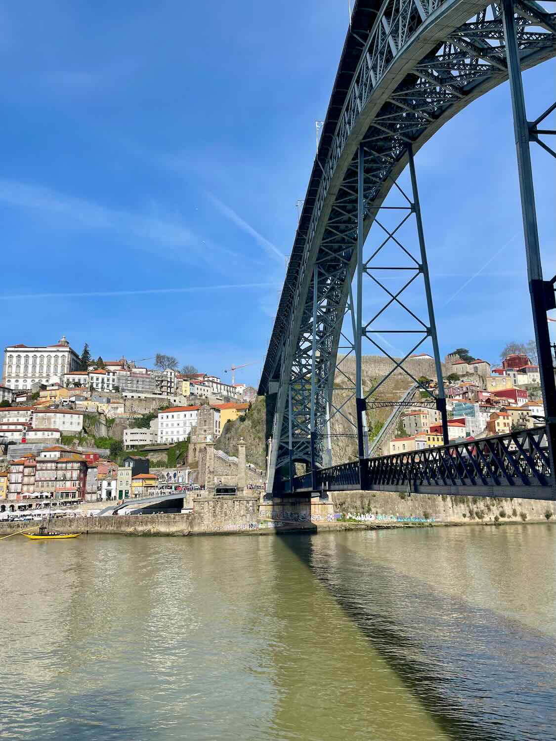 The Dom Luís I Bridge in Porto, spanning over the Douro River with the city's colorful hillside in the background.