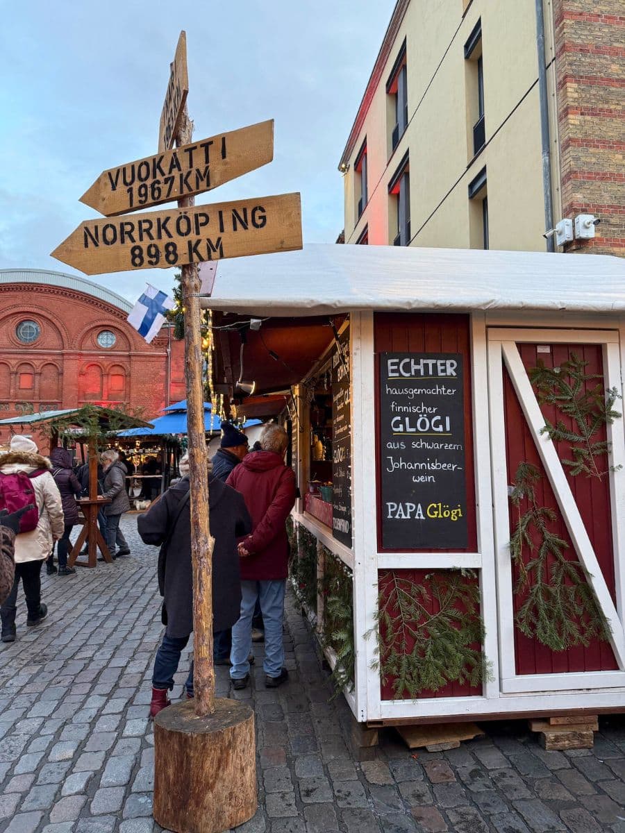A Finnish-themed Christmas market stall, featuring a wooden signpost pointing to Nordic destinations and offering homemade glögi (mulled wine).
