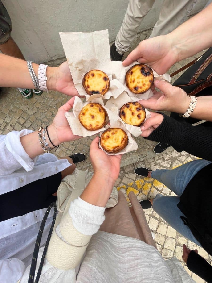 Freshly baked pastel de nata pastries on napkins, standing on a cobblestone street.