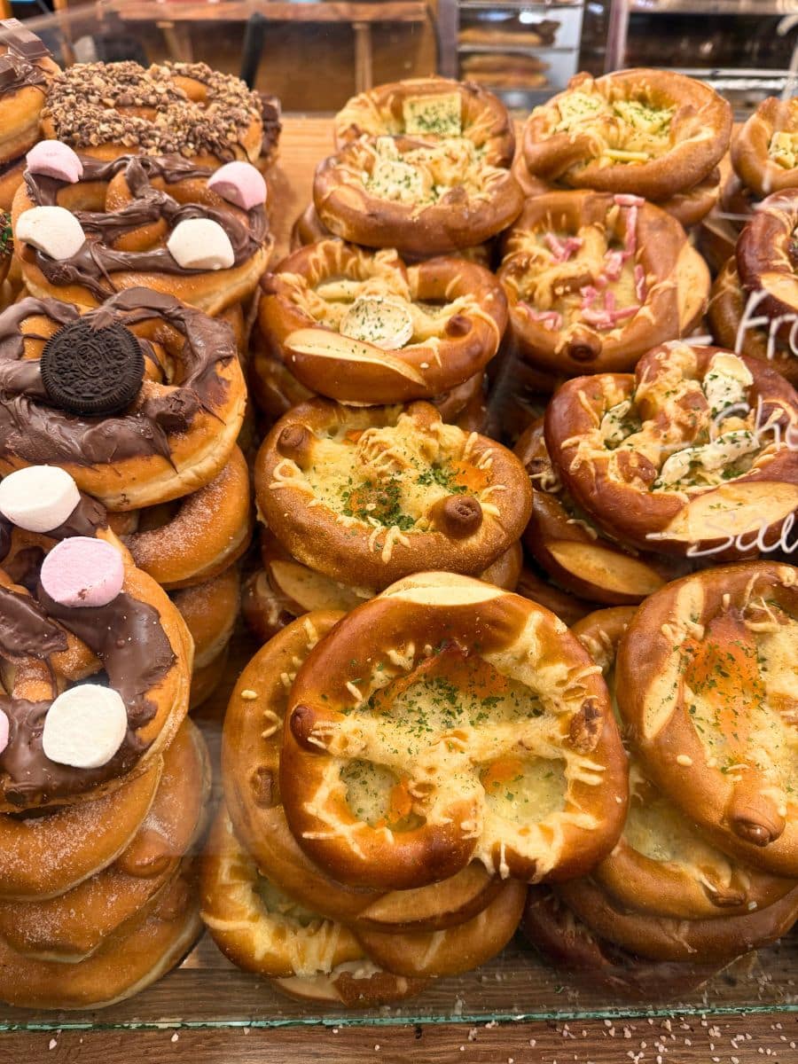 A display of freshly baked pretzels from the Strasbourg Christmas market, showcasing both savory and sweet varieties topped with ingredients like cheese, herbs, marshmallows, and chocolate.