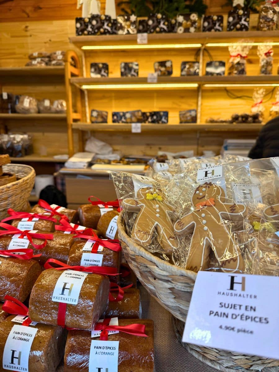 A close-up of a Christmas market stall displaying gingerbread figures and orange-spiced gingerbread loaves, wrapped with festive red ribbons, showcasing traditional holiday treats in Strasbourg.