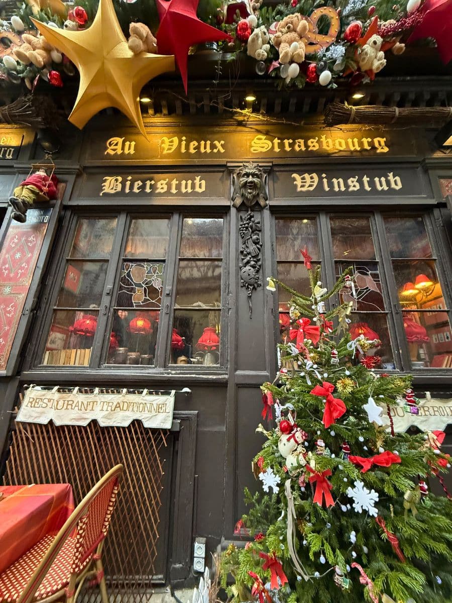 The front of "Au Vieux Strasbourg" decorated with oversized stars, plush teddy bears, and a Christmas tree adorned with red and white ornaments.
