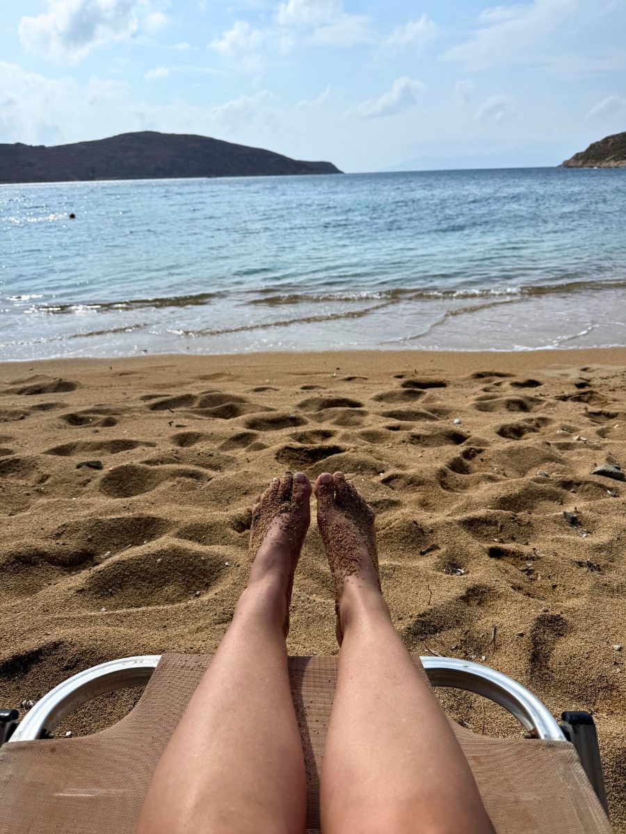 Relaxing on a sunbed with sandy feet and a view of the serene sea and hills at a beach in Serifos, Greece.