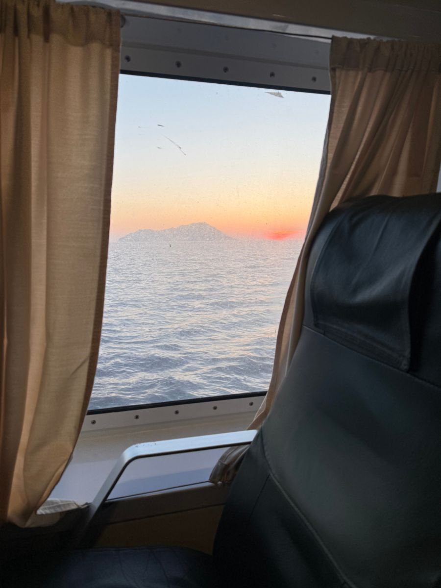 View of the ocean and a small island through a ferry window, with a pink and orange sunset in the distance.