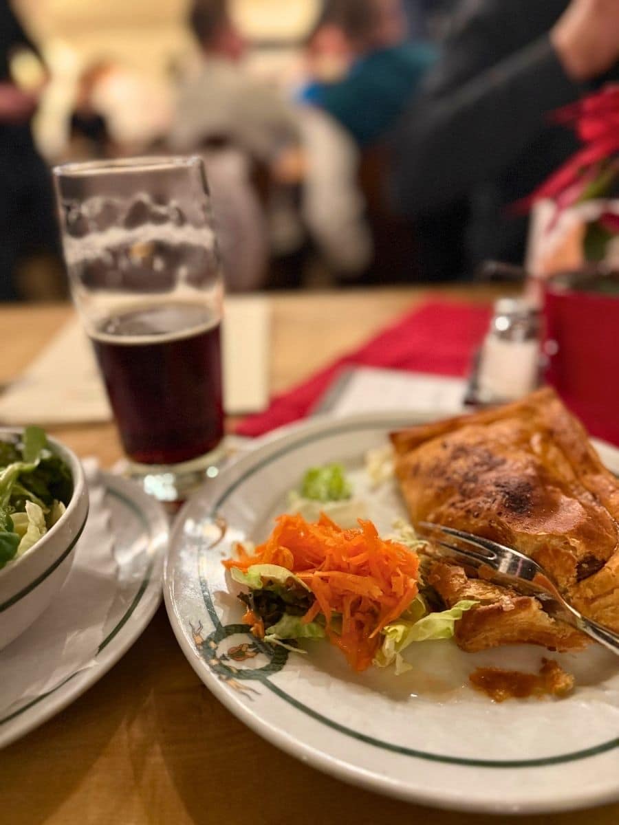 Partially eaten meal at Schlenkerla in Bamberg, showing a hearty pastry dish with shredded carrots, lettuce, and a glass of smoked beer.