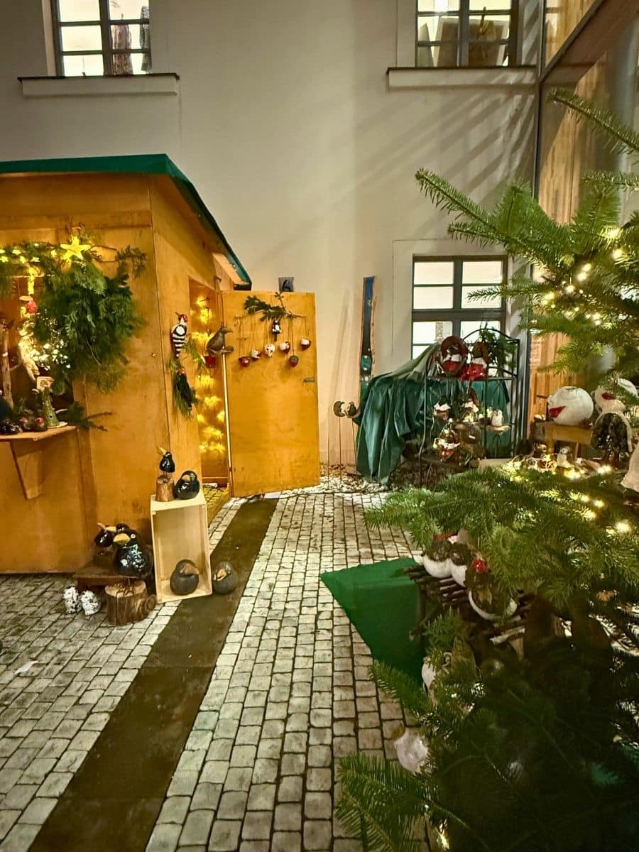 Charming Christmas market stall in Bamberg surrounded by festive greenery, ornaments, and a lit tree, set against a cobbled courtyard backdrop.