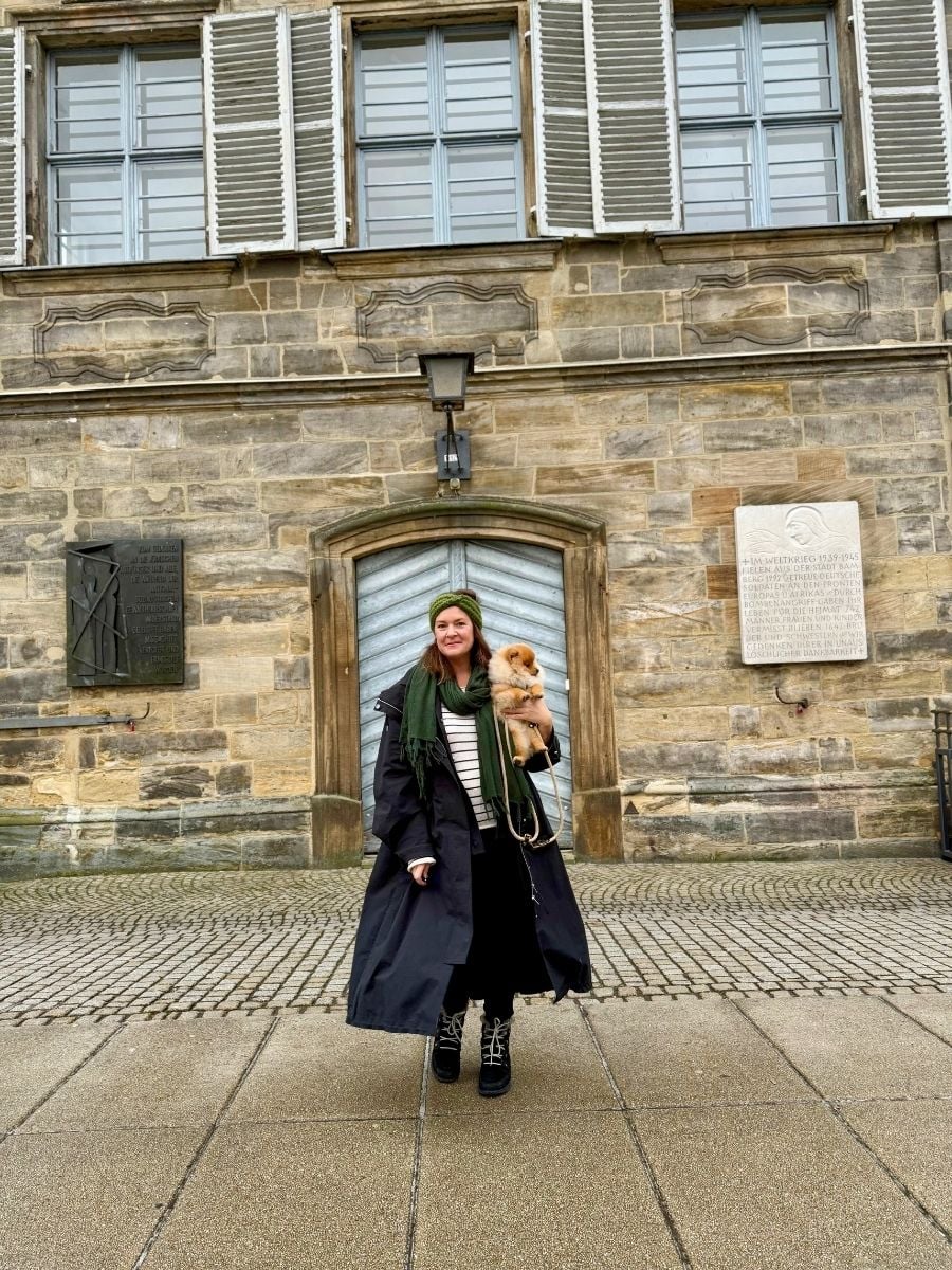 Melissa and Teddy standing directly in front of a wooden arched door with stone framing, looking straight at the camera.