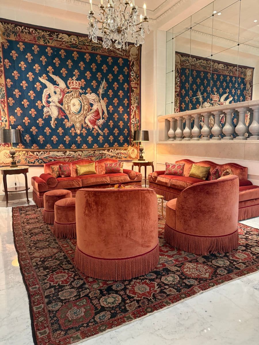Luxurious Parisian lounge with plush red velvet seating, ornate chandelier, and a royal blue tapestry with gold details.