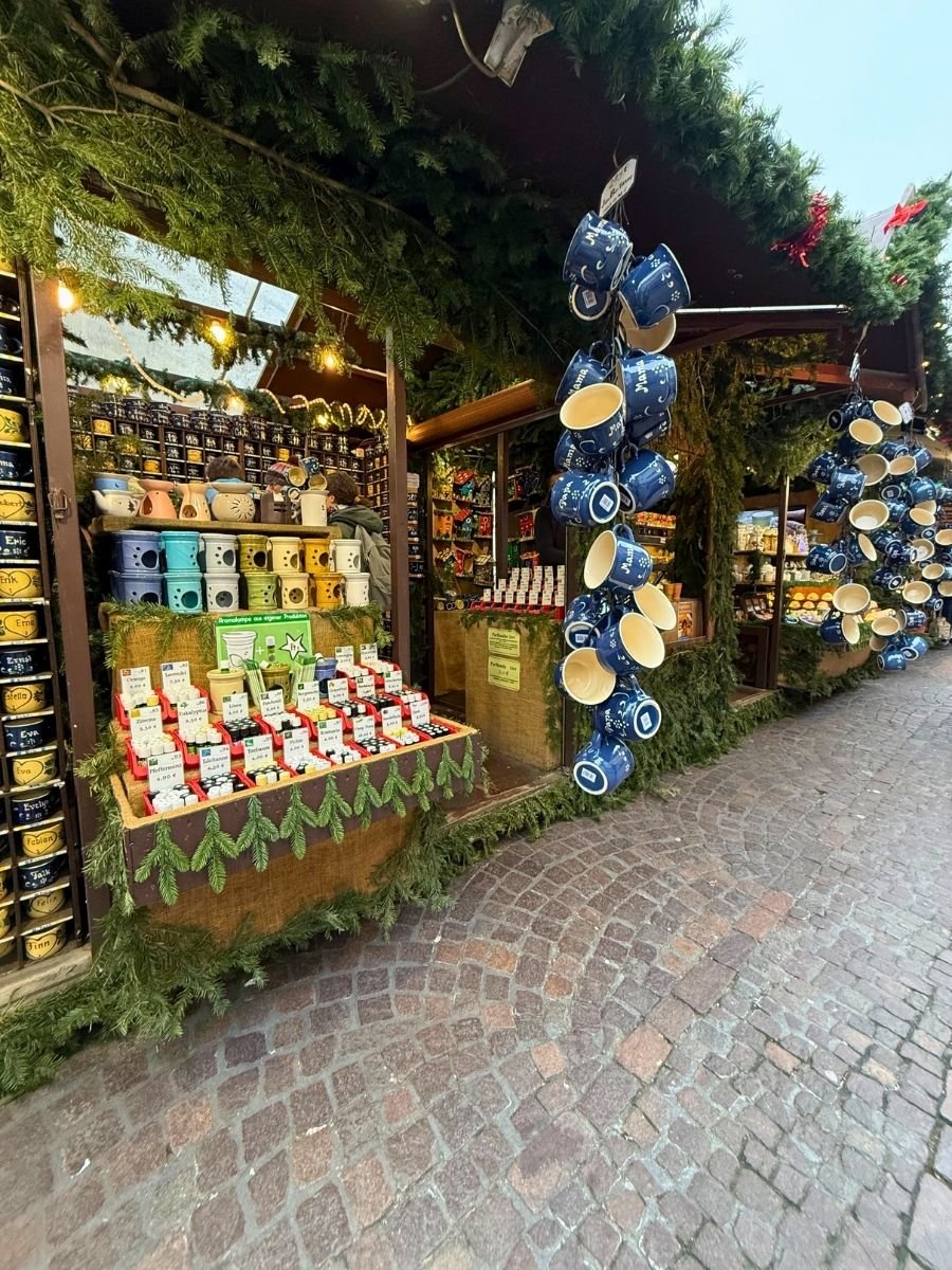 Close-up of the mug stall showing personalized name mugs, small painted ceramics, and hanging blue souvenir mugs amid Christmas greenery.