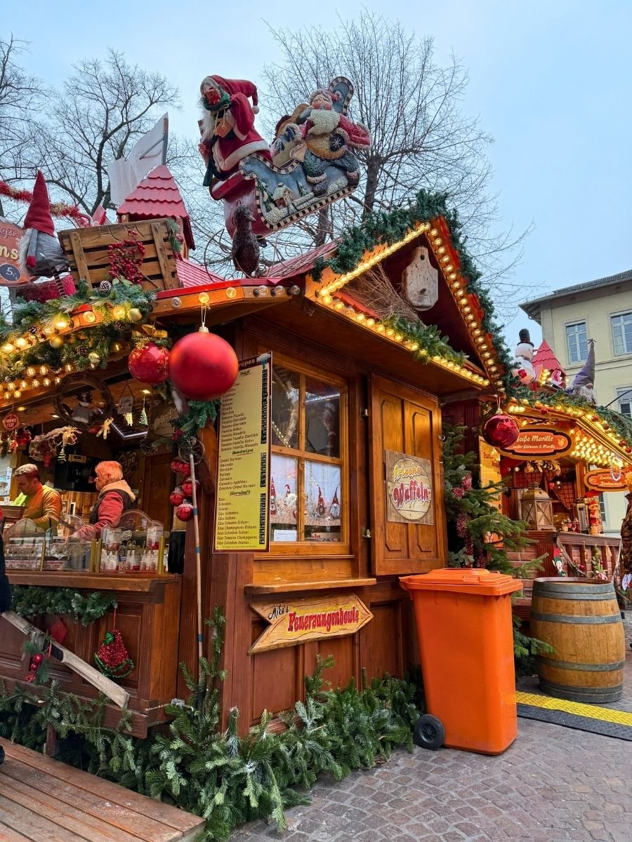 A wooden Christmas market food stall decorated with Santa figures and holiday ornaments, serving traditional German treats like Feuerzangenbowle.