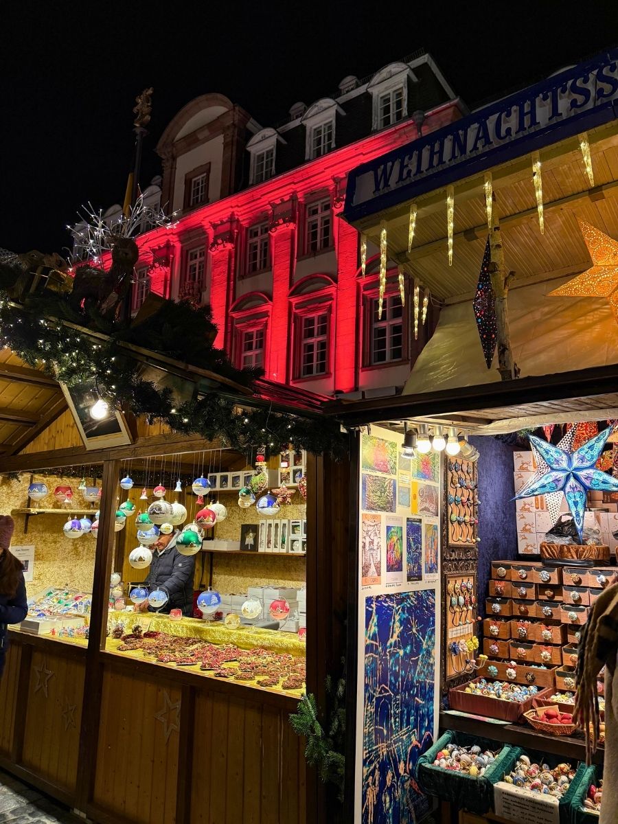 Colorful Christmas market stalls selling ornaments and crafts with a red-lit building behind.