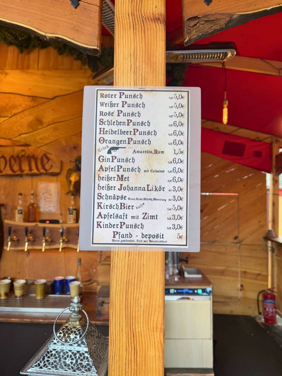 A close-up of a wooden post displaying a menu of various hot punch drinks including Roter, Weißer, Heidelbeer, and Apfelpunsch, with prices listed in euros.