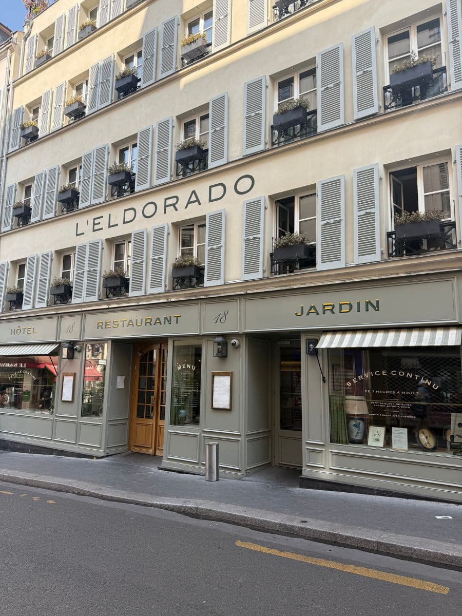 Facade of Hotel Eldorado Paris with rows of shuttered windows, black flower boxes, and signage for the hotel, restaurant, and garden.