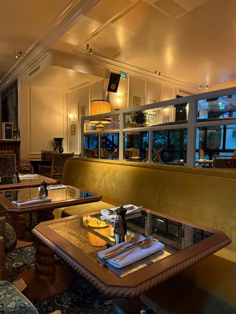 Warmly lit dining area at Hotel Eldorado Paris with velvet banquette seating, glass-top tables, and cozy ambient lighting.