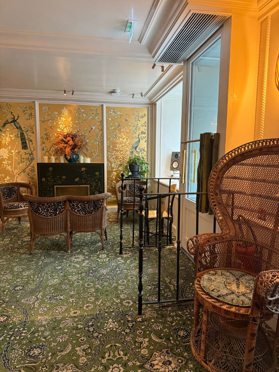 Elegant hotel lounge at Hotel Eldorado Paris featuring wicker furniture, green patterned carpet, and gold-accented wall panels with bird motifs.
