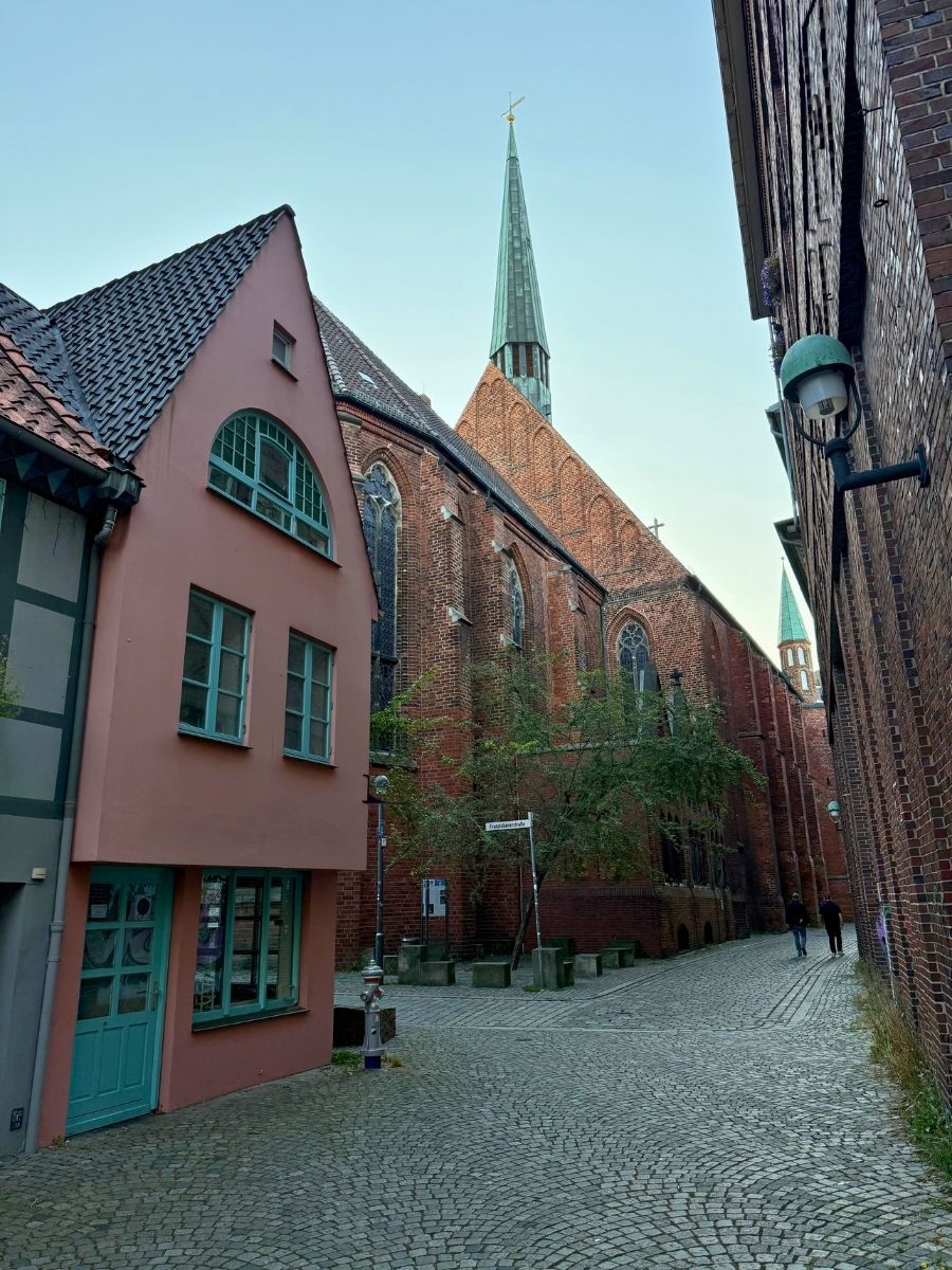 A quiet cobblestone street in Bremen’s old town, with charming houses and the Gothic spire of St. John’s Church in the background.