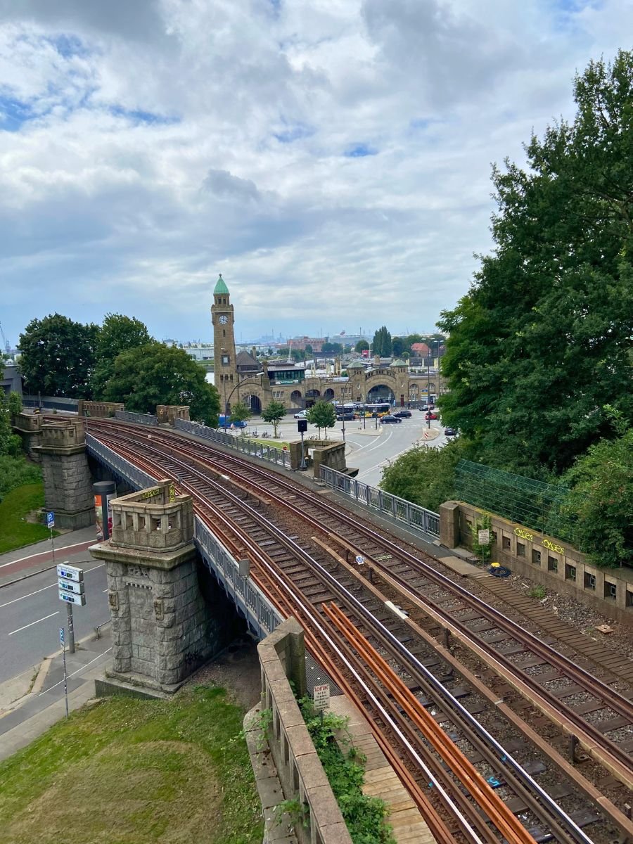 The railway tracks lead toward the historic Landungsbrücken (St. Pauli Piers), one of Hamburg’s most iconic landmarks. With its clock tower in the distance and the harbor nearby, this spot highlights the city’s strong maritime identity.