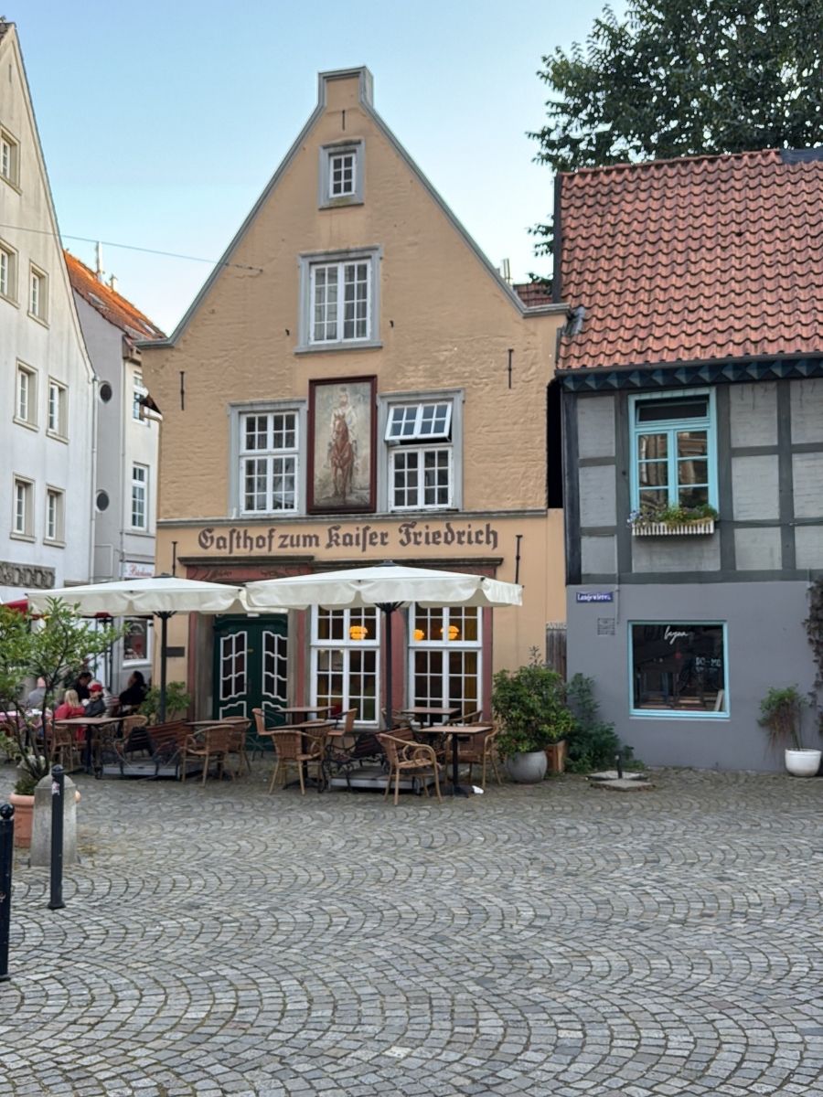 A charming view of Gasthof zum Kaiser Friedrich in Bremen&rsquo;s Schnoor quarter, a historic inn with outdoor seating and classic German cuisine.