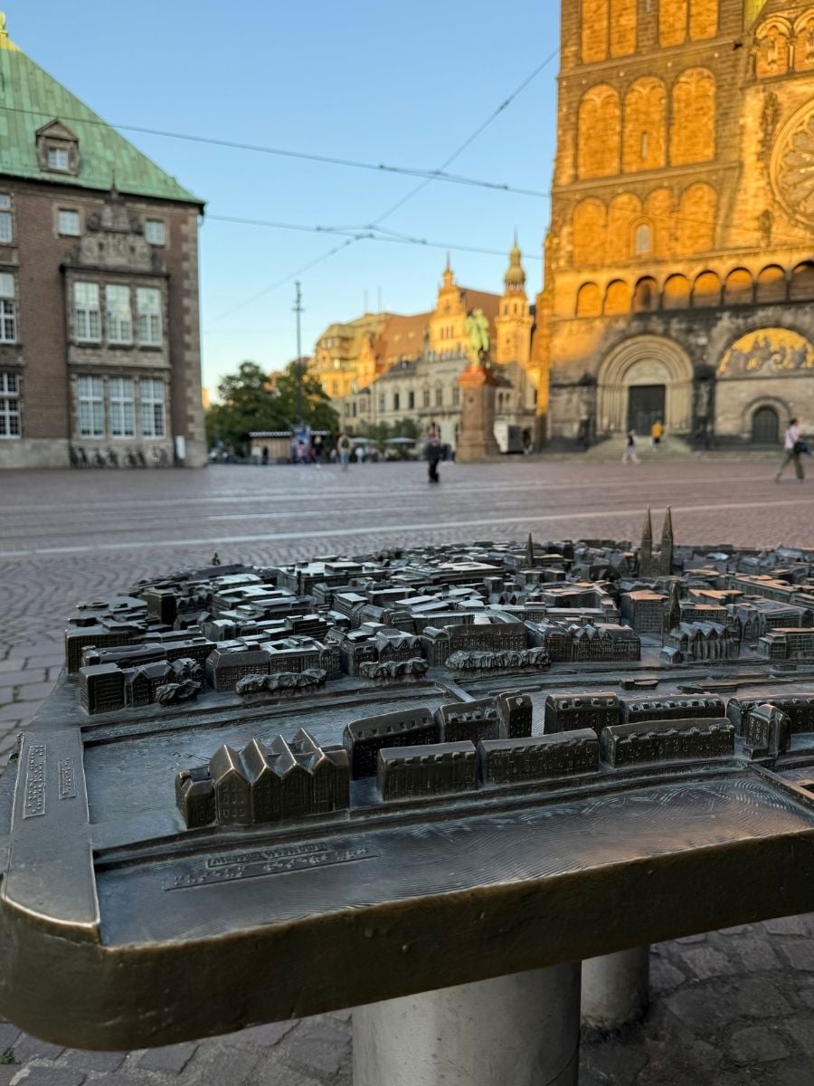 A detailed bronze city model of Bremen displayed in the Marktplatz, with the UNESCO-listed Town Hall and historic cathedral glowing in the evening light.