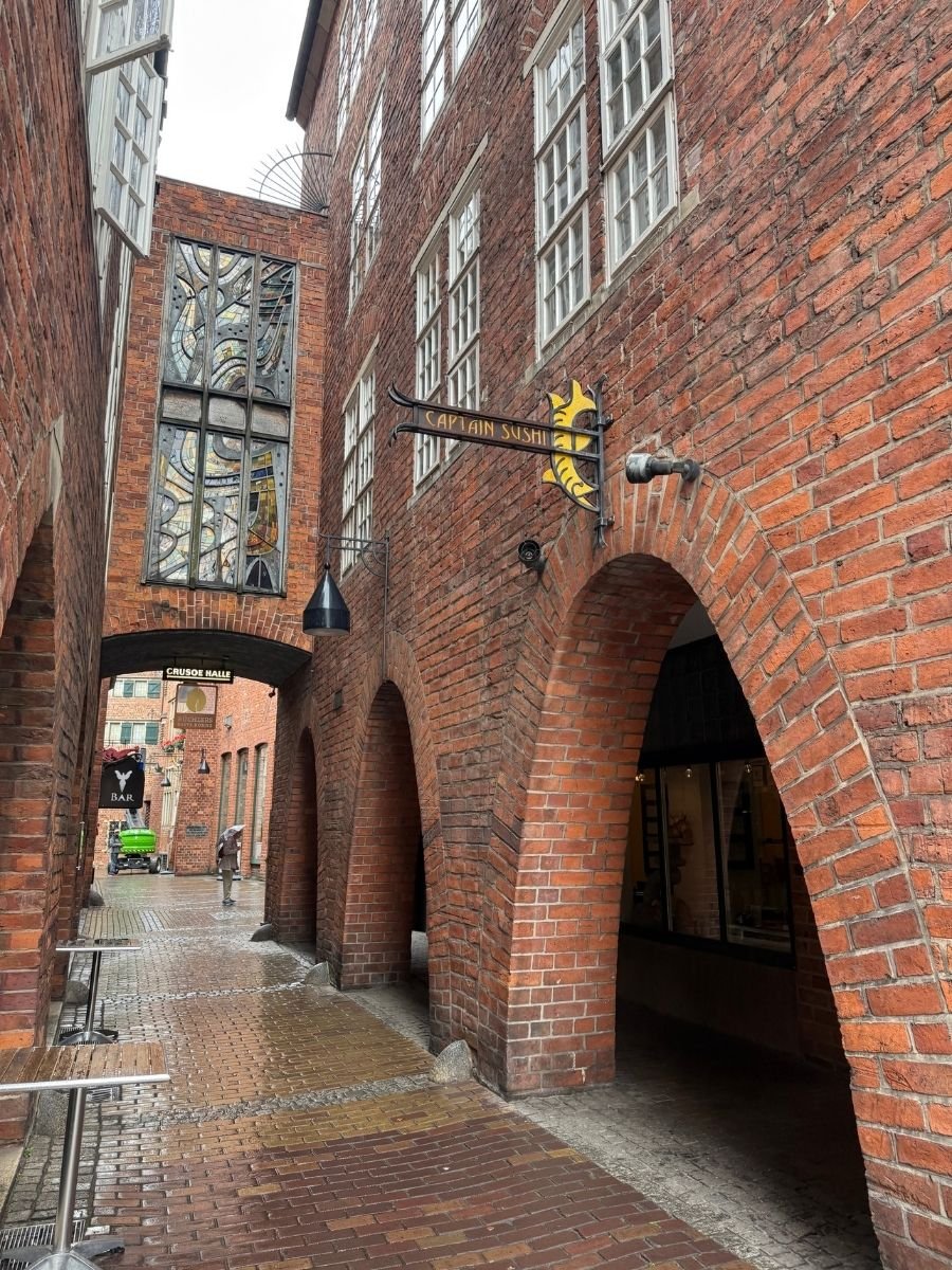Red brick archway with stained glass window and “Captain Sushi” sign in Böttcherstraße, Bremen.