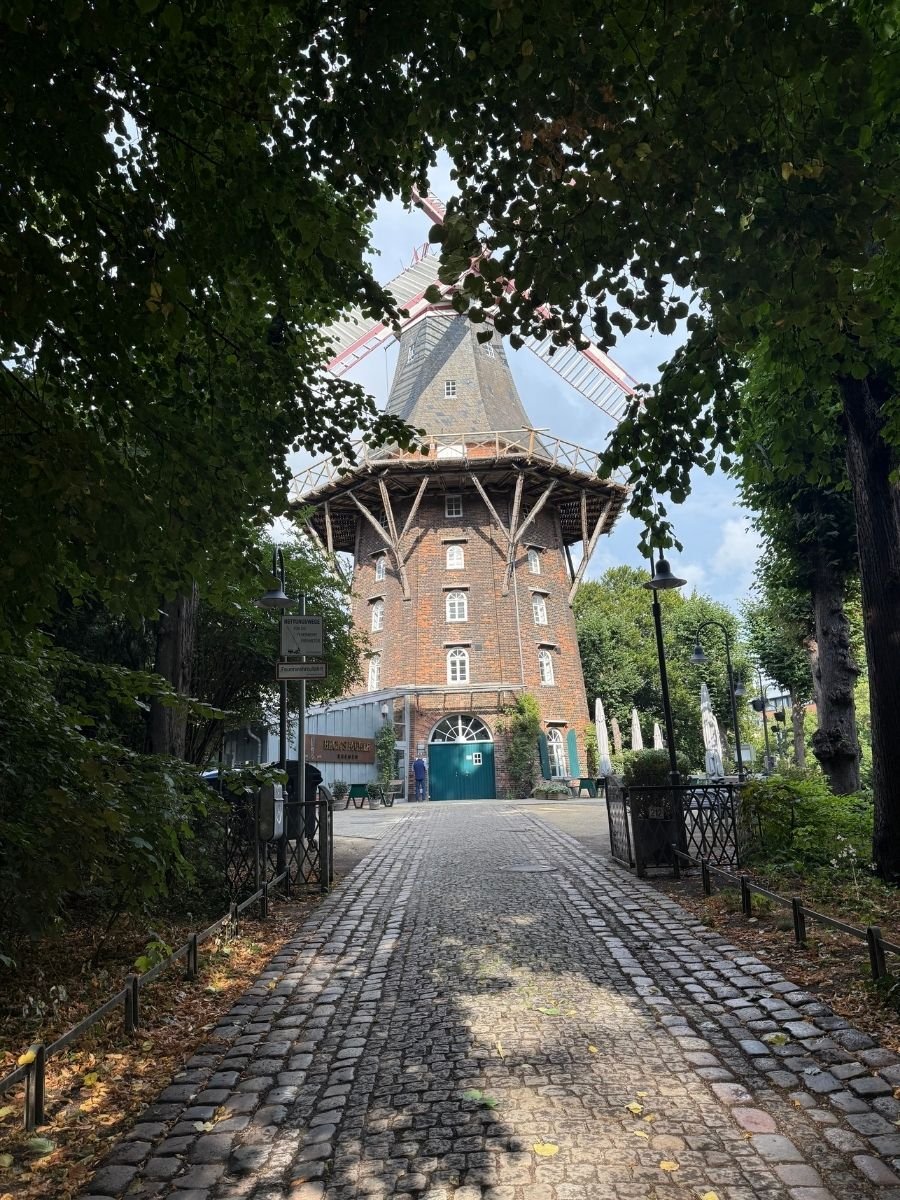 Pathway framed by trees leading to the front of a traditional brick windmill in Bremen, Germany.