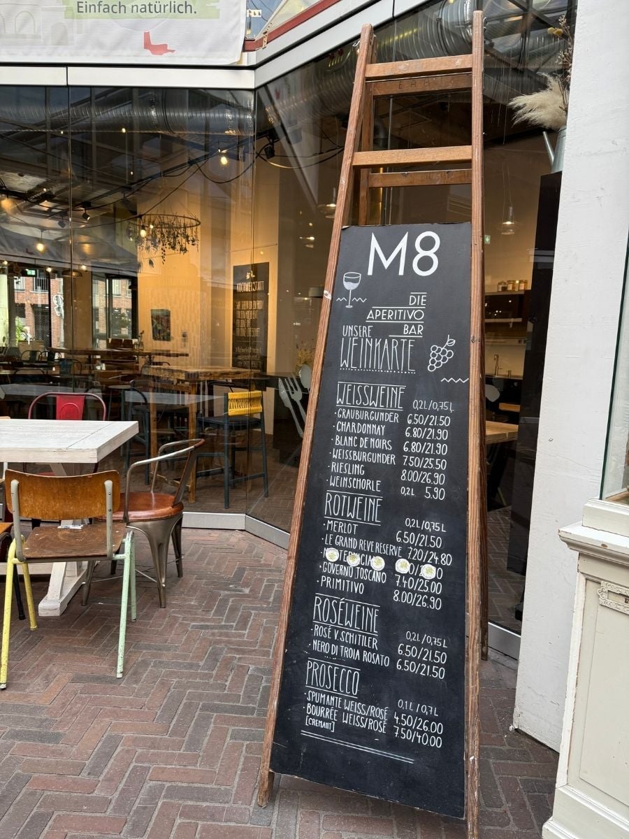 Chalkboard wine menu outside M8 Aperitivo Bar at Markthalle Acht in Bremen, Germany, listing white, red, ros&eacute; wines, and prosecco.