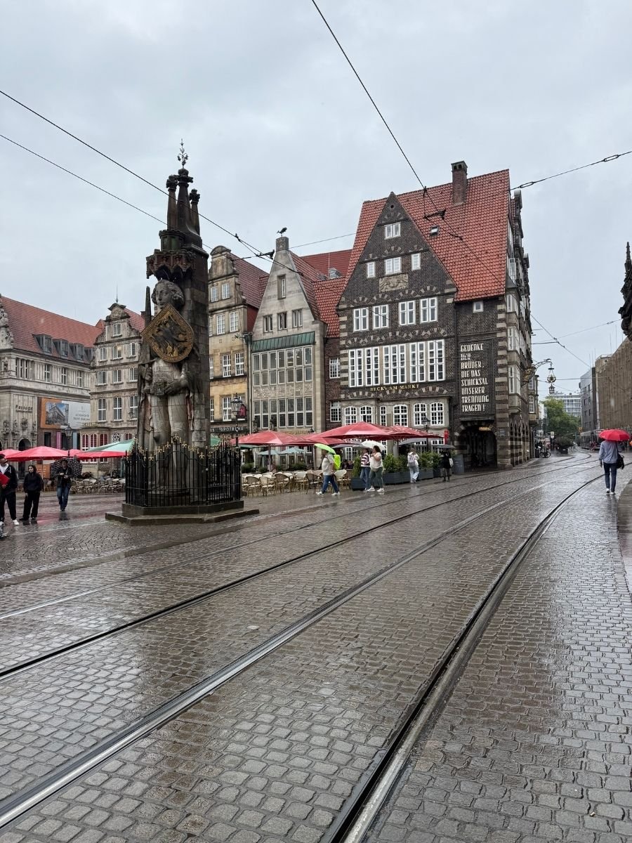 Large medieval Roland statue holding a shield in Bremen’s market square, surrounded by half-timbered buildings and tram tracks.