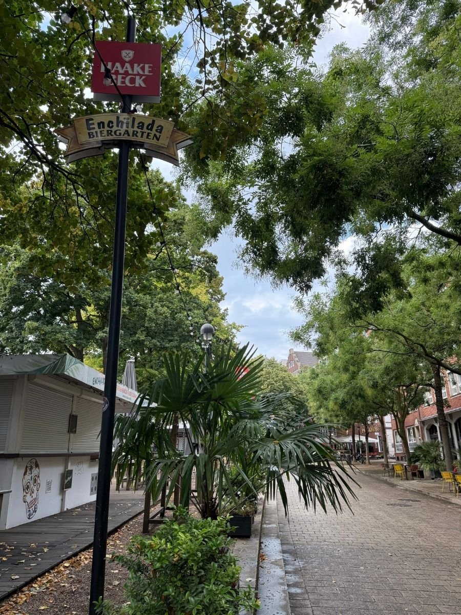 The leafy entrance to Enchilada Biergarten in Bremen, marked by the Haake Beck beer sign and shaded by tropical-style greenery.