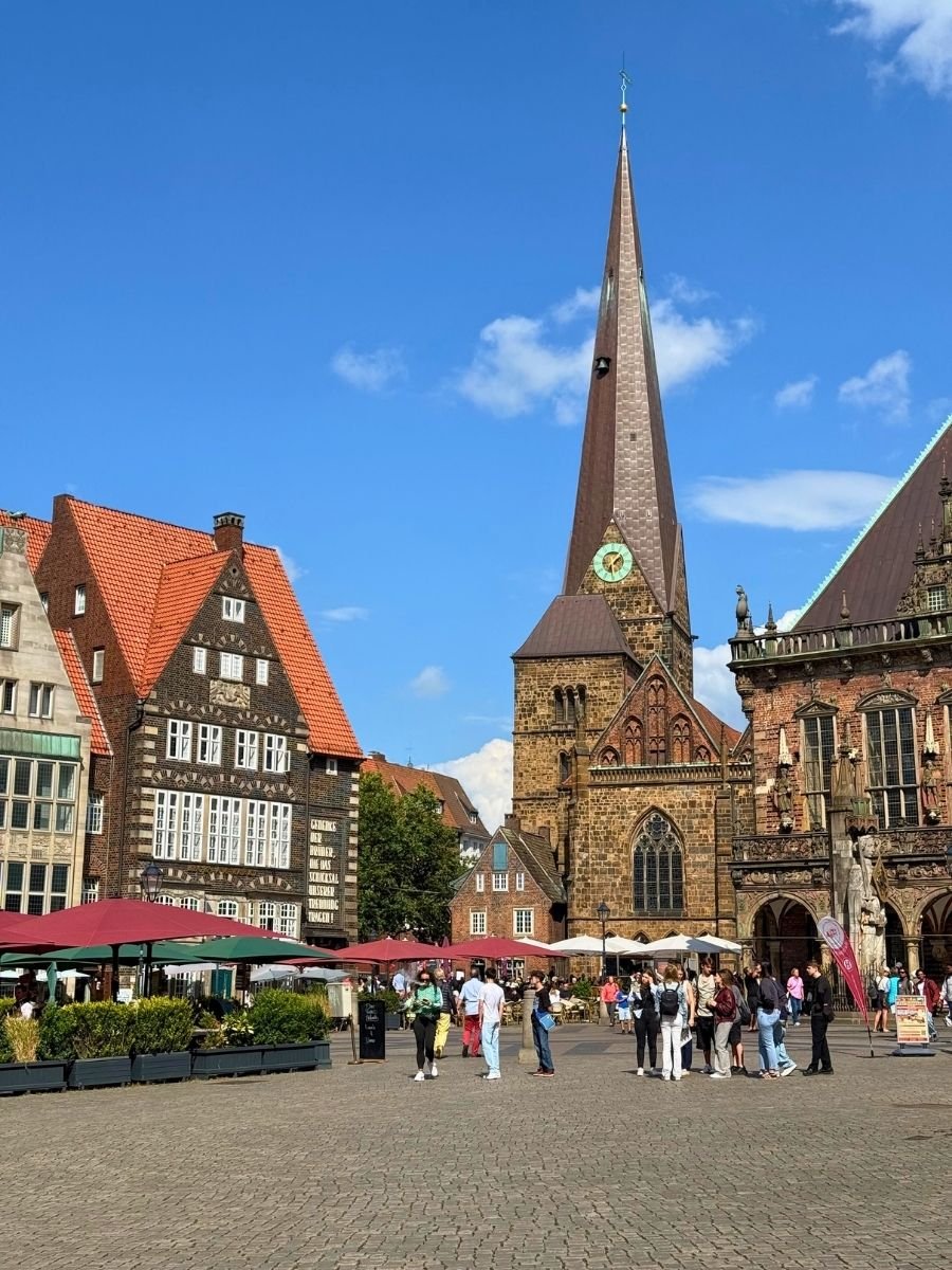 A closer look at Bremen’s Marktplatz featuring the tall spire of St. Martin’s Church, charming gabled houses, and vibrant outdoor cafés under red umbrellas.