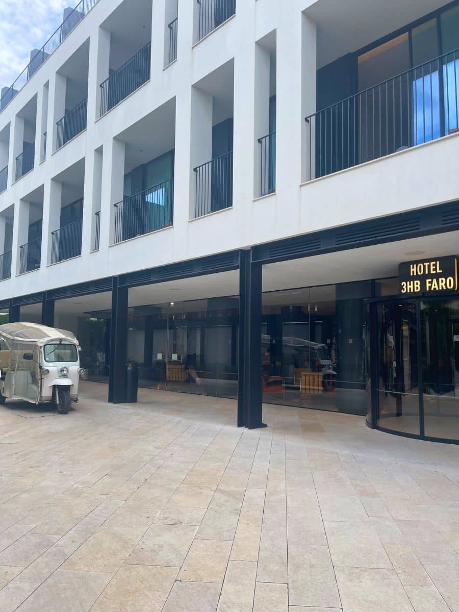 Modern white facade of 3HB Faro with balconies and a tuk-tuk parked outside.