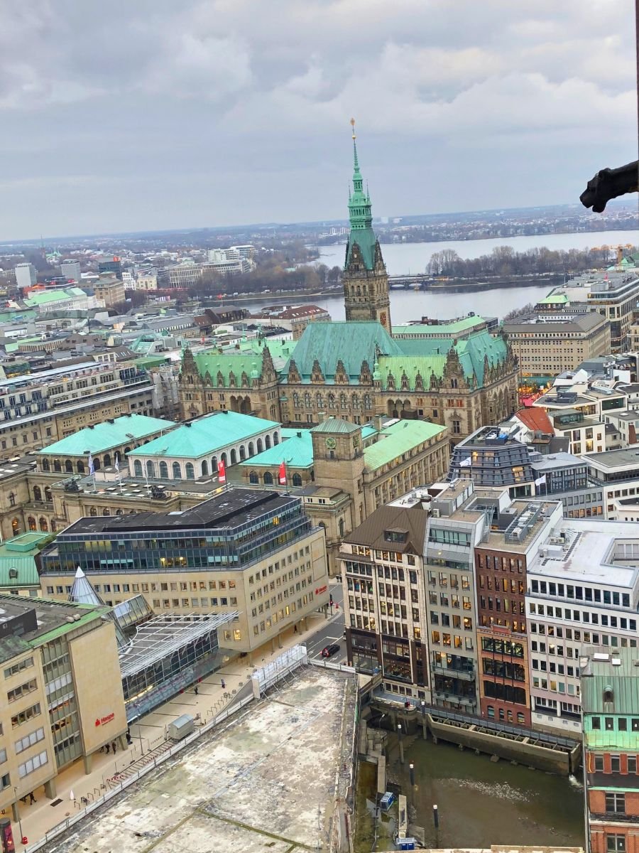 A breathtaking aerial view of Hamburg shows the Rathaus surrounded by the city’s rooftops and waterways. The panoramic scene captures Hamburg’s mix of historic landmarks and modern life.