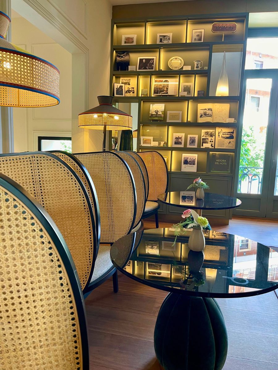 Elegant lounge with rattan-backed chairs, glass tables, and illuminated shelving with decor and history displays.