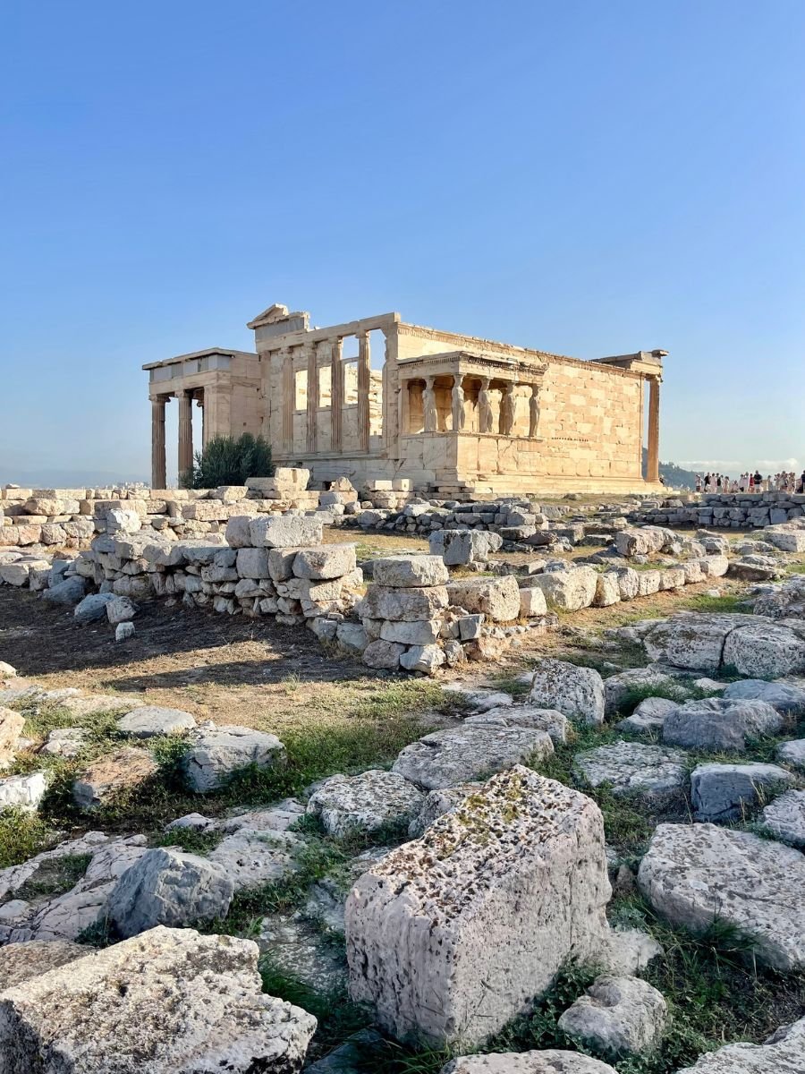Ancient Erechtheion temple ruins with iconic Caryatids, located on the Acropolis hill under clear blue skies.