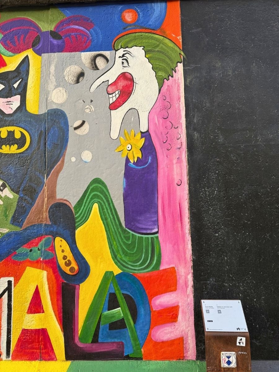 Close-up of a brightly colored section of the East Side Gallery mural, featuring Batman and The Joker with exaggerated features, in Berlin.
