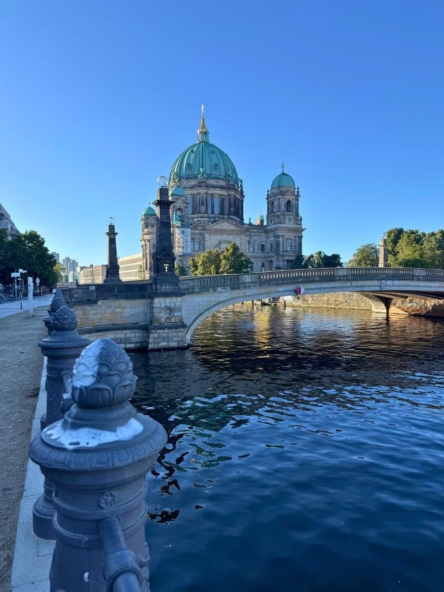 View of Berlin Cathedral and the bridge over the Spree River in Berlin on a bright sunny day, with reflections shimmering on the water.