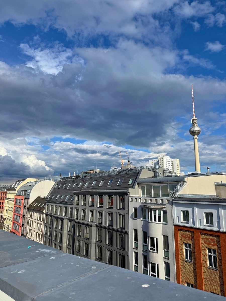 Rooftop cityscape view of Berlin with the Fernsehturm TV Tower rising under dramatic clouds.