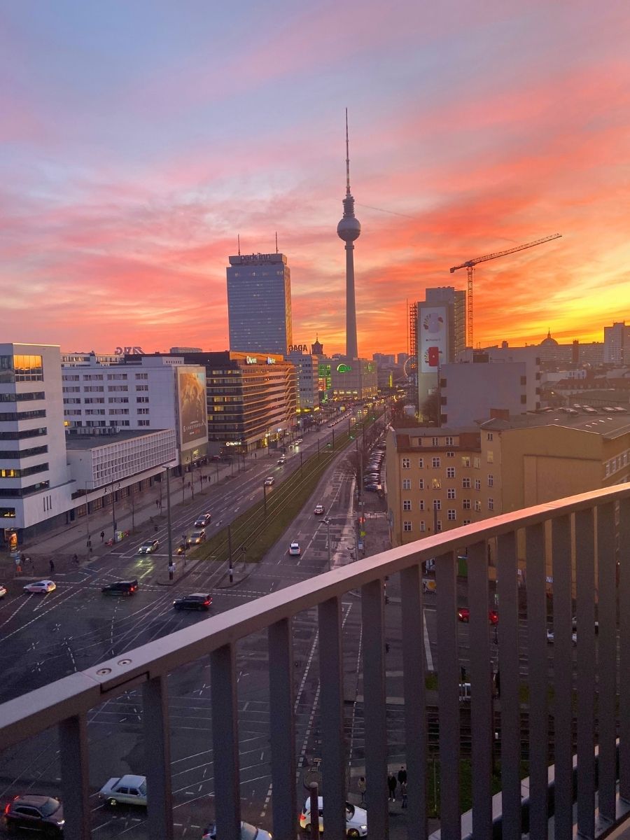 Berlin skyline at sunset with the Fernsehturm TV Tower glowing against vibrant pink and orange clouds.