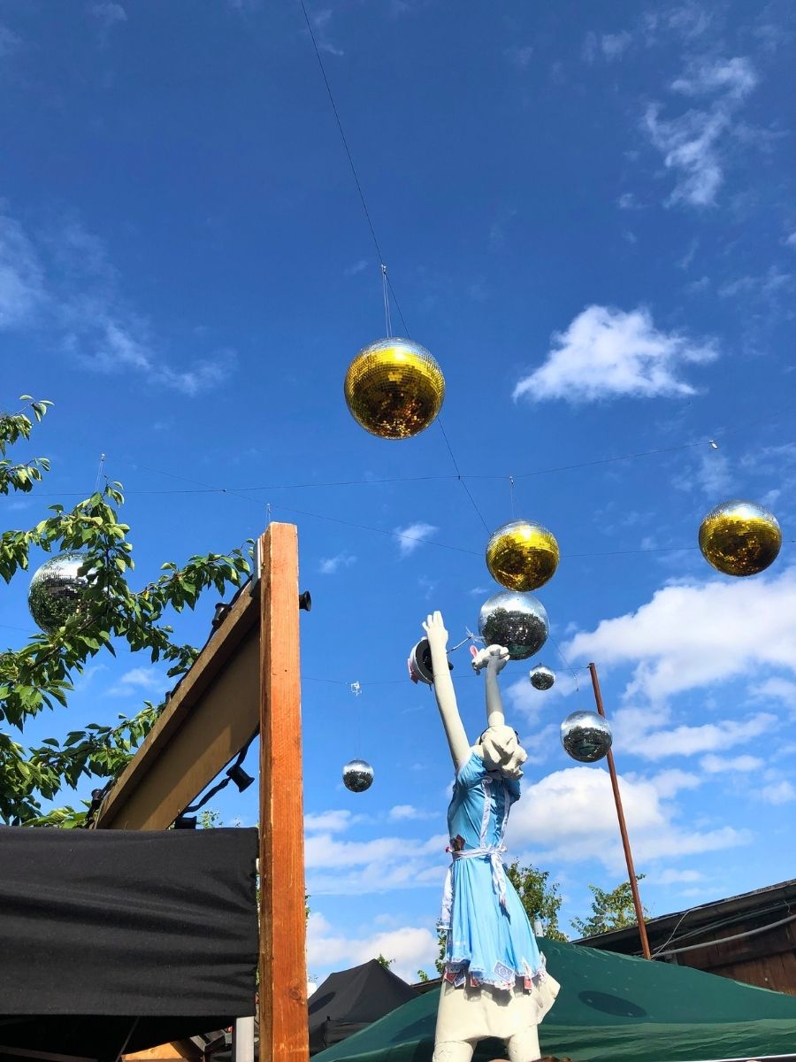 Decorative mannequin in a blue dress reaching toward hanging disco balls at an outdoor space in Berlin.