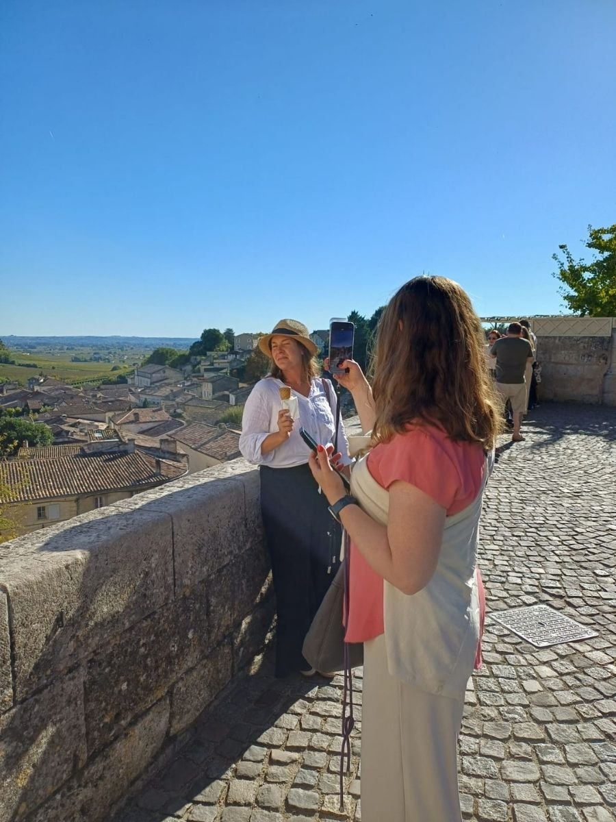 A woman poses for a photo with gelato at a scenic overlook in Saint-Émilion, Bordeaux, with rooftops and vineyards in the background.