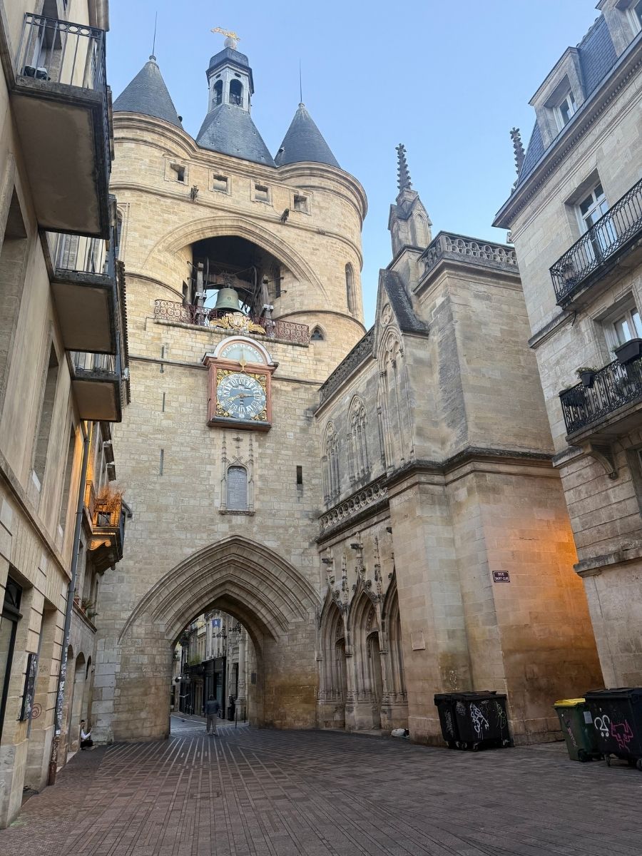 Historic Grosse Cloche bell tower and archway in the old town of Bordeaux, France, captured during early morning with empty cobblestone street and clear blue sky.